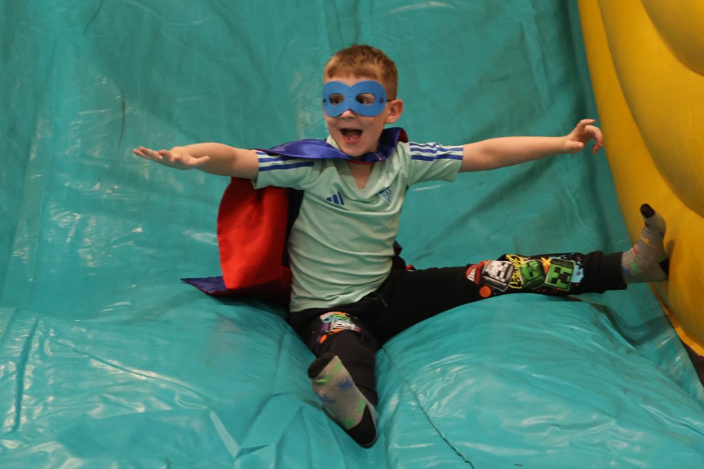 Child dressed as superhero enjoying an inflatable slide.