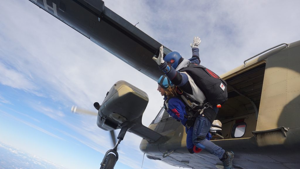 Two people jumping out of a plane, taking part in a tandem skydive in the air