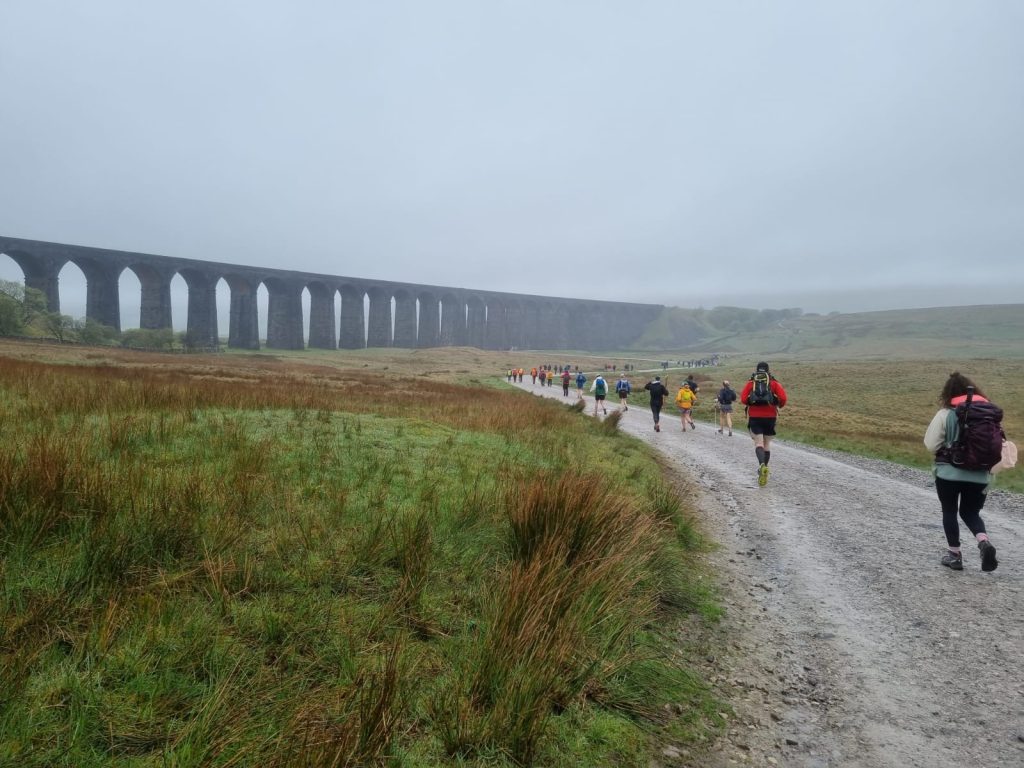 View of Yorkshire Three Peaks walkers in the countryside near a large bridge