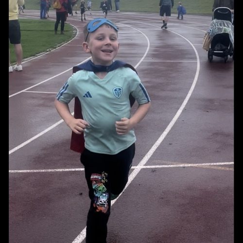 Young boy wearing superhero mask and cape, running on a race track