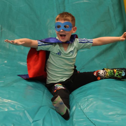 Child dressed as superhero enjoying an inflatable slide.